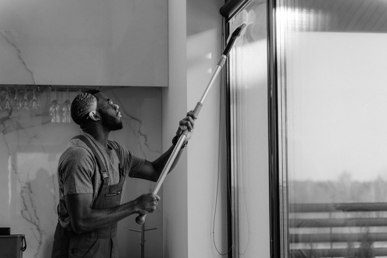 Un homme nettoyant une fenêtre en verre avec une raclette, en noir et blanc, mettant en valeur un travail professionnel.